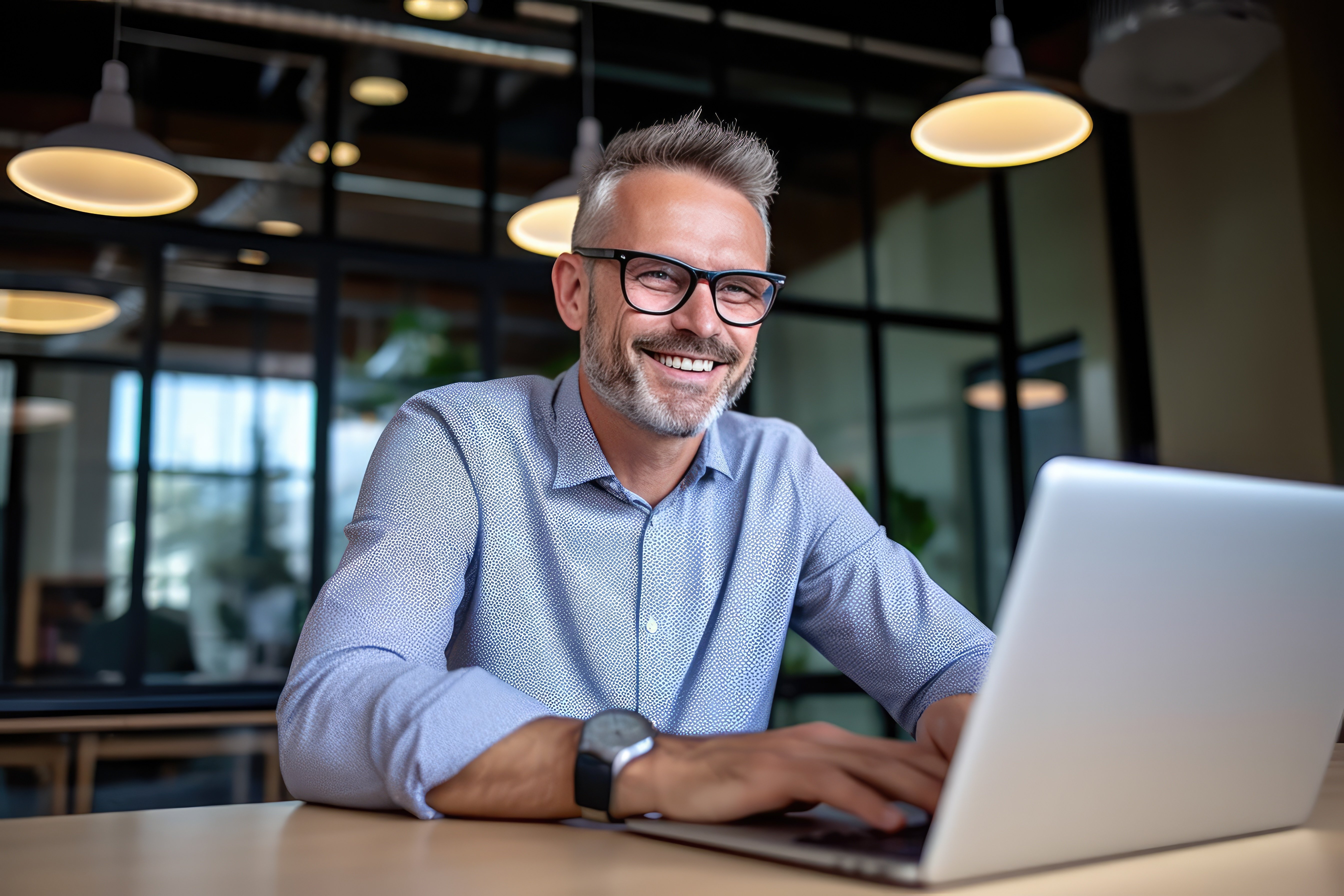 Grey haired man with glasses reviewing material on laptop